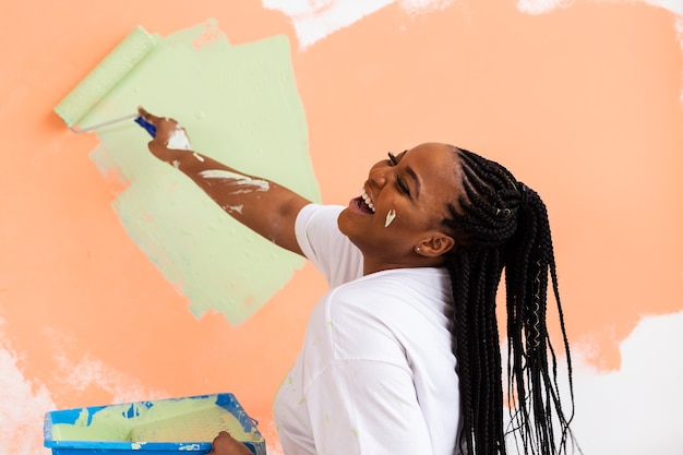 Mujer afro pintando las paredes del nuevo hogar. Concepto de renovación, reparación y redecoración.