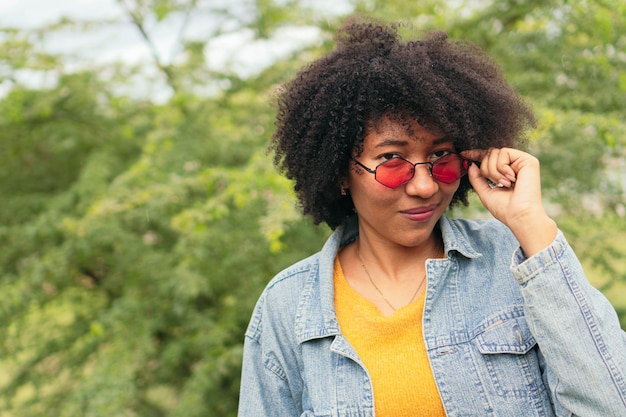 Mujer afro posando al aire libre con plantas verdes en el fondo