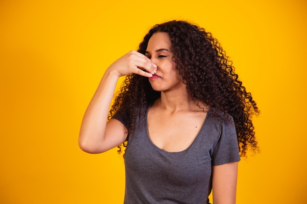 Mujer afro que se siente disgustada, tapándose la nariz para evitar oler un hedor desagradable y desagradable