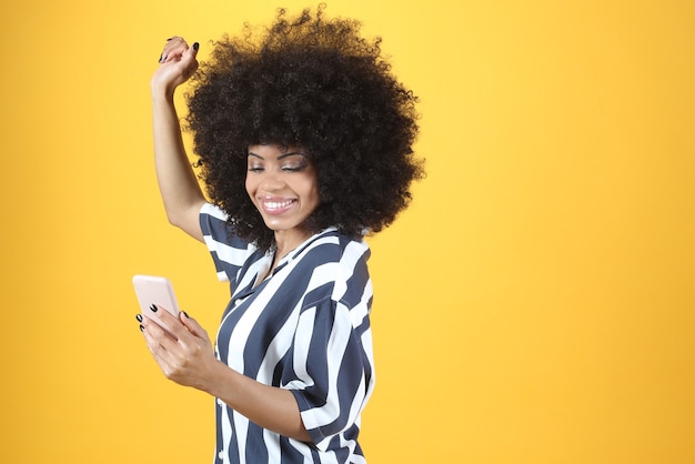 Mujer afro, con smartphone bailando sobre fondo amarillo