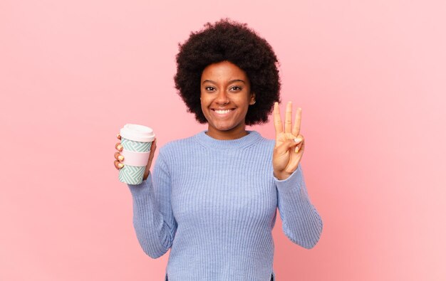 Mujer afro sonriendo y luciendo amigable, mostrando el número tres o tercero con la mano hacia adelante, contando hacia atrás. concepto de cafe