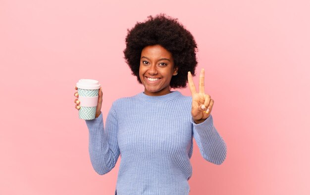 mujer afro sonriendo y luciendo feliz, despreocupada y positiva, gesticulando victoria o paz con una mano. concepto de cafe