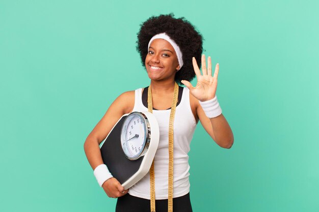 Mujer afro sonriendo y mirando amigable, mostrando el número cinco o quinto con la mano hacia adelante, contando el concepto de dieta