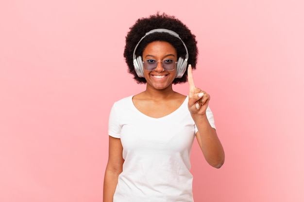 Mujer afro sonriendo y mirando amigable, mostrando el número uno o primero con la mano hacia adelante, contando hacia atrás. concepto de musica