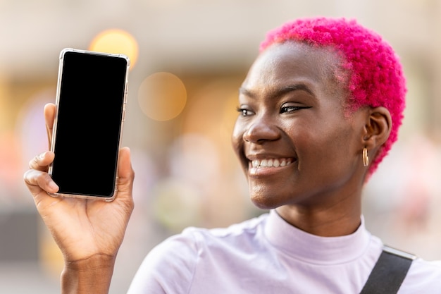 Mujer afro sonriente que muestra la pantalla de un móvil al aire libre