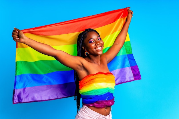 Mujer afro sosteniendo la bandera del orgullo LGBT en el fondo azul del estudio