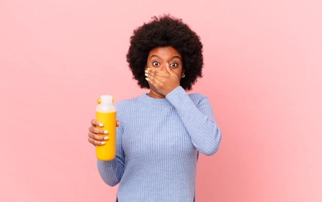 Mujer afro tapándose la boca con las manos con una expresión de asombro, sorpresa, guardando un secreto o diciendo uy. concepto de batido