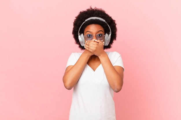 mujer afro tapándose la boca con las manos con una expresión de sorpresa y sorpresa, guardando un secreto o diciendo uy. concepto de musica