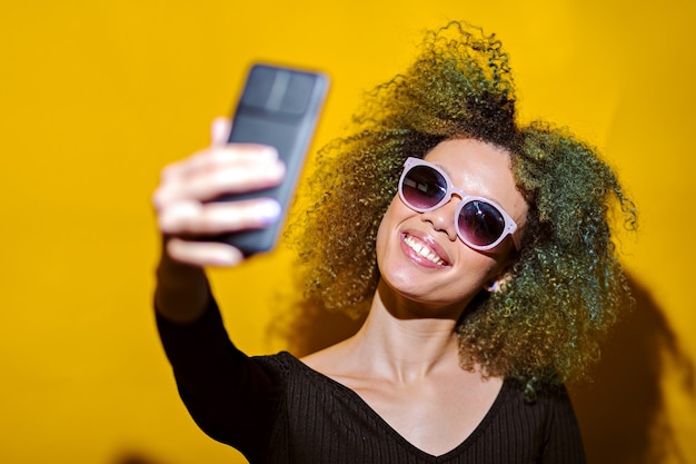 Mujer afro toma selfie con gafas de sol sobre fondo amarillo