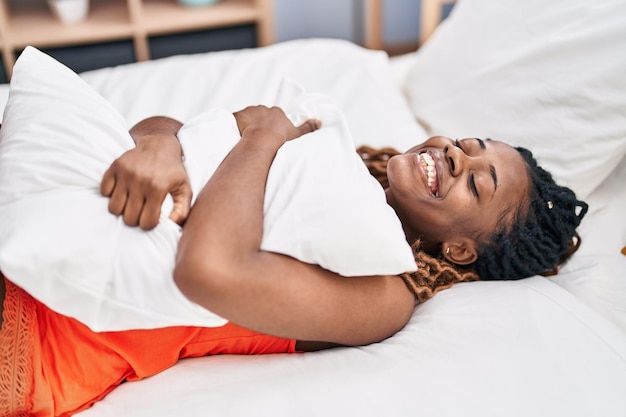 Mujer afroamericana abrazando almohada acostada en la cama en el dormitorio