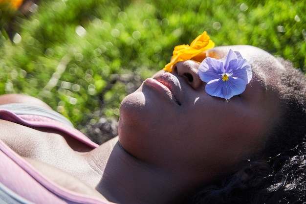 mujer afroamericana acostada en la hierba con dos flores cubriendo sus ojos