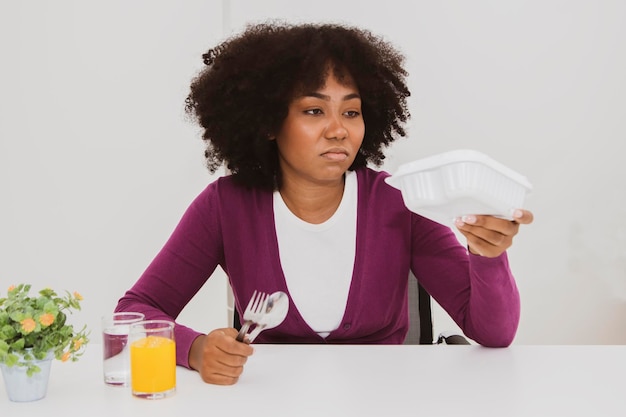 La mujer afroamericana adolescente lleva comida en caja del supermercado parece harta de la mala nutrición