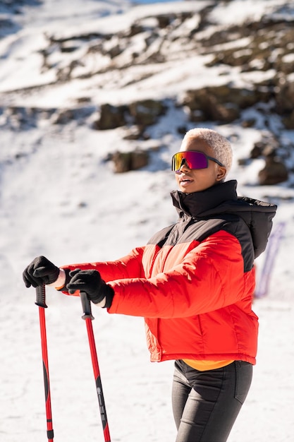 Una mujer afroamericana con bastones de esquí de pie sobre una montaña nevada durante el invierno