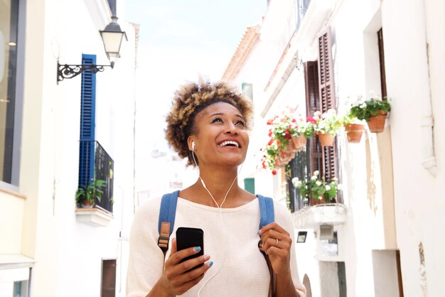 Mujer afroamericana caminando por la calle y escuchando música en el teléfono móvil