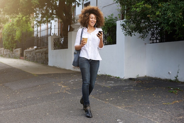 Mujer afroamericana caminando y mirando el teléfono móvil