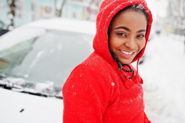 Mujer afroamericana en coche limpio con capucha roja de la nieve en día de invierno.