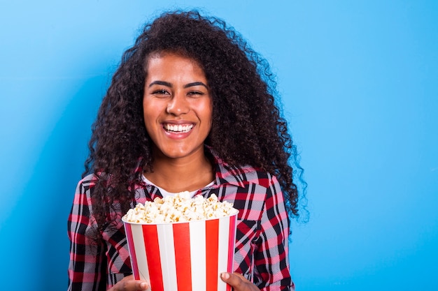 Mujer afroamericana comiendo palomitas de maíz feliz con gran sonrisa