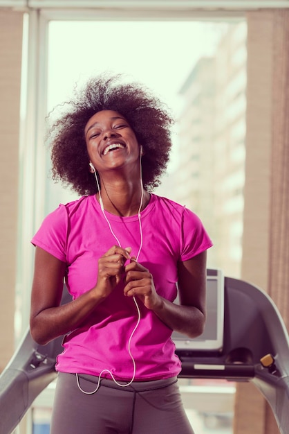 mujer afroamericana corriendo en una cinta de correr en el gimnasio mientras escucha música en los auriculares