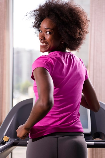 mujer afroamericana corriendo en una cinta de correr en el gimnasio mientras escucha música en los auriculares