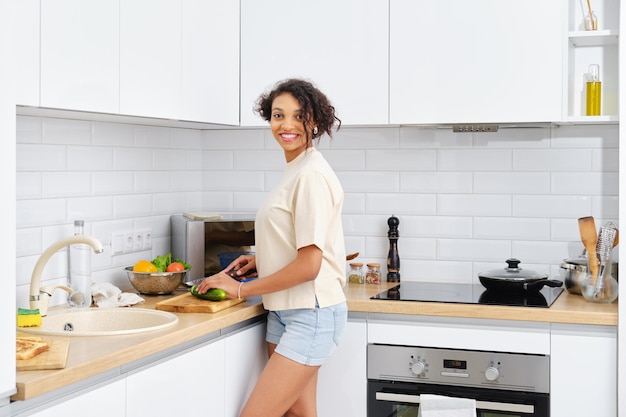 Mujer afroamericana corta un pepino para una ensalada y se distrae cuando alguien entra a la cocina