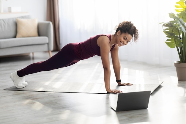 Mujer afroamericana delgada positiva haciendo ejercicio en casa usando computadora