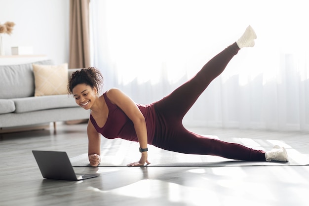 Mujer afroamericana deportiva haciendo ejercicio en casa usando una computadora portátil