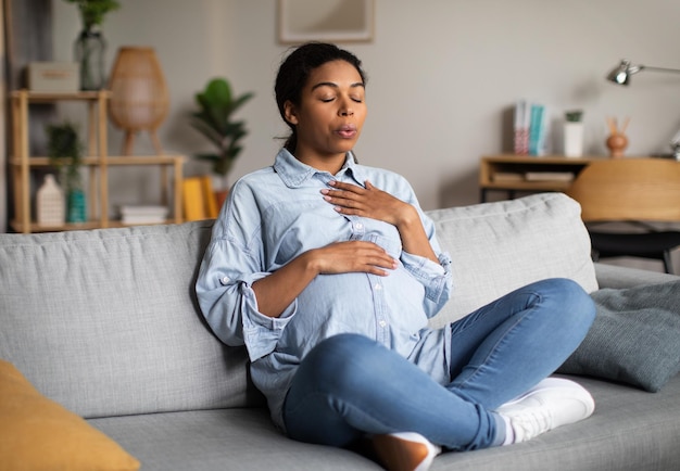 Mujer afroamericana embarazada haciendo ejercicio de respiración sentado en casa