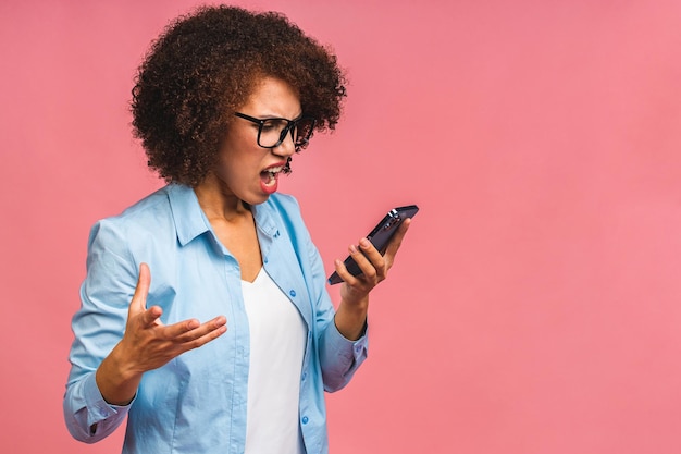 Mujer afroamericana enojada gritando en el teléfono móvil aislada sobre fondo rosa