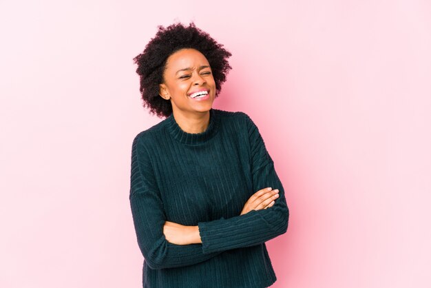Mujer afroamericana envejecida media contra una pared rosada que ríe y que se divierte.