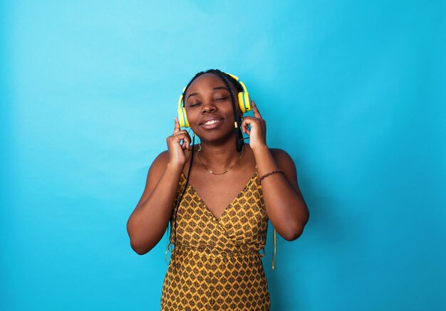 Una mujer afroamericana escucha música con auriculares amarillos en un fondo azul.