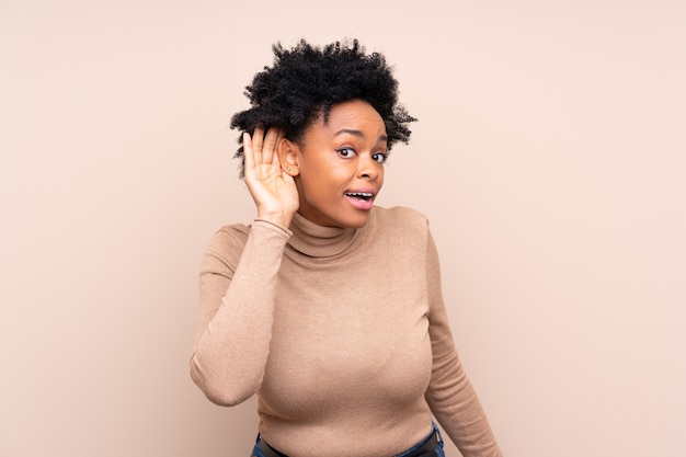 Mujer afroamericana escuchando algo poniendo la mano en la oreja