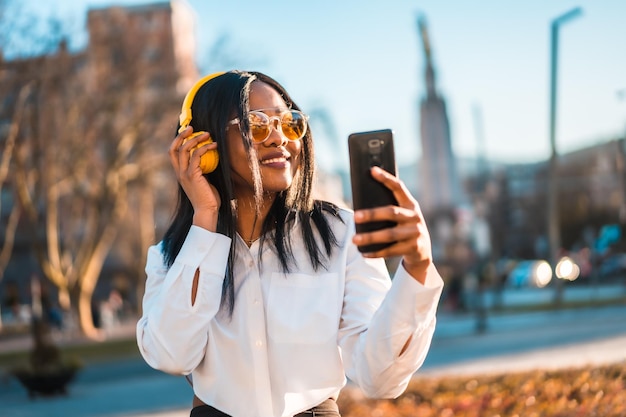 Mujer afroamericana escuchando música con auriculares al atardecer en la ciudad transmitiendo música