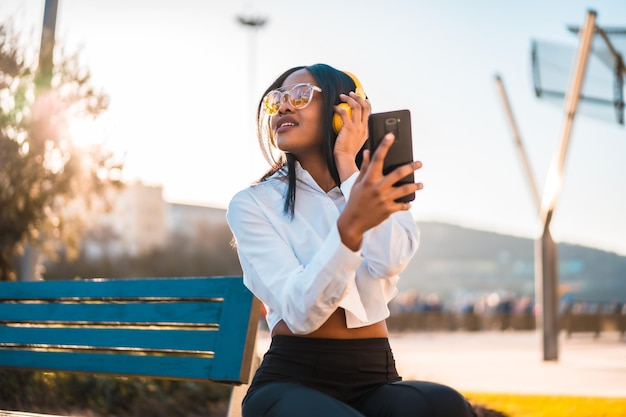 Mujer afroamericana escuchando música con auriculares al atardecer en la ciudad