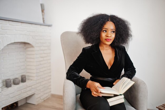 Mujer afroamericana con estilo en negro posó en la habitación contra la chimenea leer libros