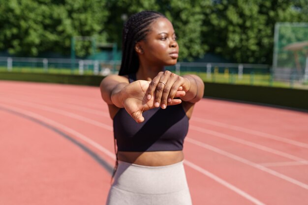 Mujer afroamericana estira las manos calentándose antes de un entrenamiento intensivo en un día soleado de verano