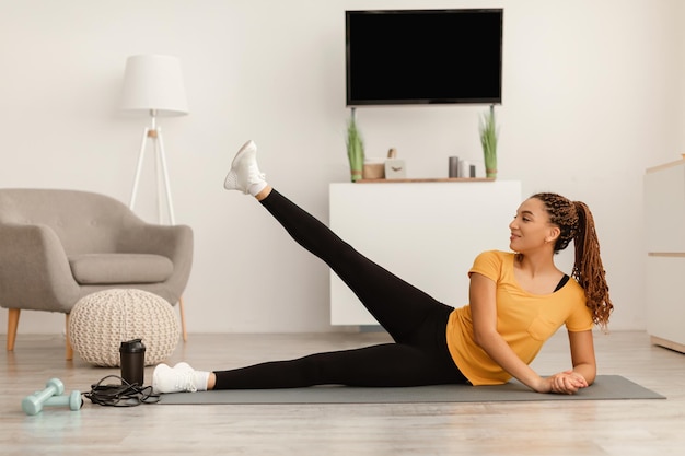 Mujer afroamericana feliz haciendo levantamientos de piernas laterales en casa