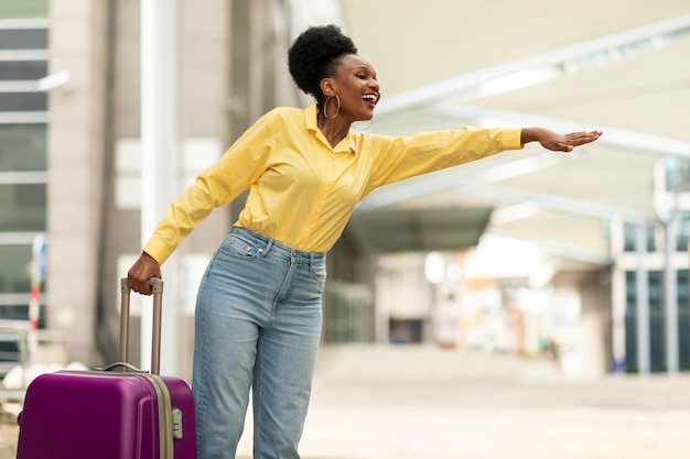 Mujer afroamericana feliz llamando a un taxi parado cerca del aeropuerto