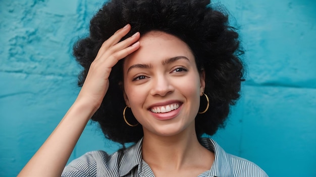 Una mujer afroamericana feliz toca la frente, inclina la cabeza y sonríe felizmente a la cámara.