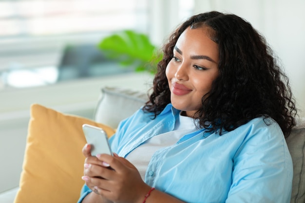 Mujer afroamericana feliz usando mensajes de texto de teléfono inteligente en casa