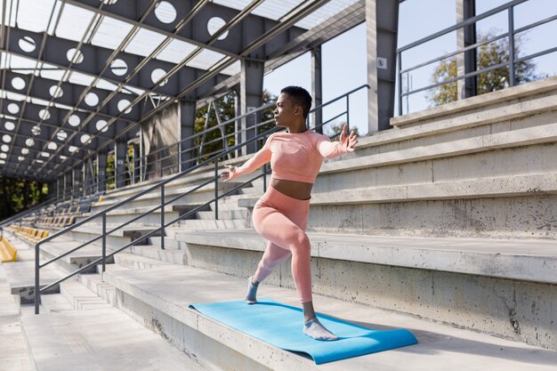 Mujer afroamericana haciendo yoga cerca del estadio por la mañana, estilo de vida activo realiza ejercicios de fitness