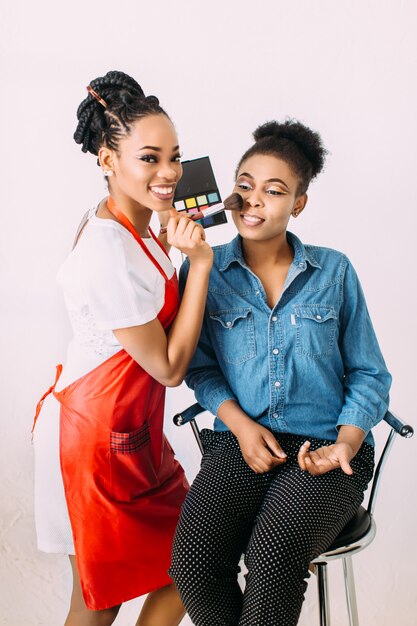 Mujer afroamericana hermosa joven que aplica maquillaje profesional por el artista de maquillaje africano. Sesión de estudio