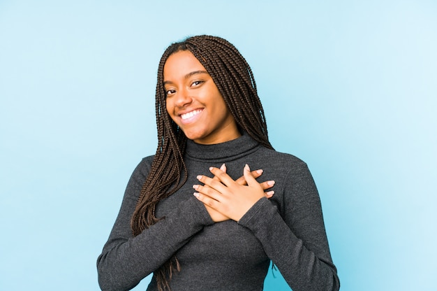 La mujer afroamericana joven aislada en la pared azul tiene expresión amistosa, presionando la palma al pecho. Concepto de amor