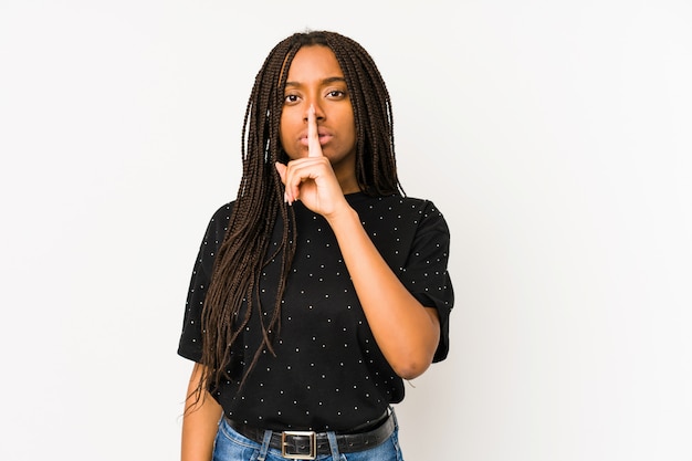 Mujer afroamericana joven aislada en la pared blanca que guarda un secreto o que pide silencio.