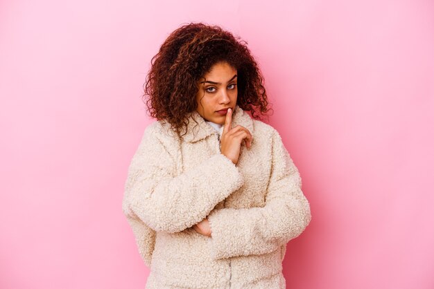 Mujer afroamericana joven aislada en la pared rosada infeliz con expresión sarcástica.