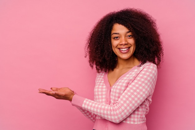 Mujer afroamericana joven aislada en la pared rosada que sostiene un espacio de la copia en una palma.