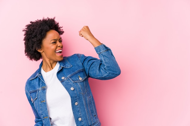 La mujer afroamericana joven contra un backgroound rosado aisló levantar el puño después de una victoria, concepto del ganador.