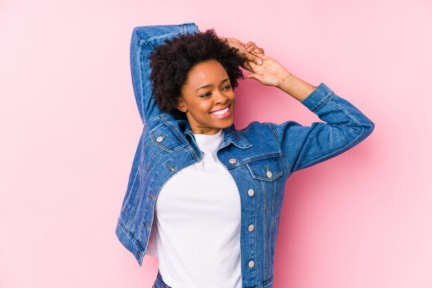 Mujer afroamericana joven contra una pared rosada que estira los brazos, posición relajada.