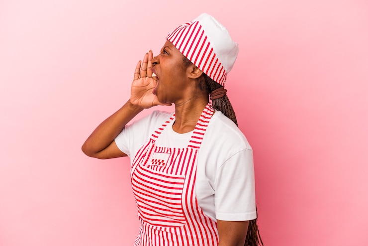 Foto mujer afroamericana joven fabricante de helado aislada sobre fondo rosa gritando y sosteniendo la palma cerca de la boca abierta.
