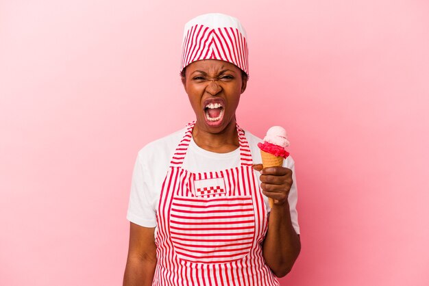 Mujer afroamericana joven fabricante de helado sosteniendo helado aislado sobre fondo rosa gritando muy enojado y agresivo.