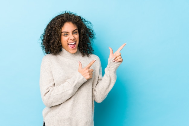 Mujer afroamericana joven del pelo rizado que señala con los dedos índices a un espacio en blanco